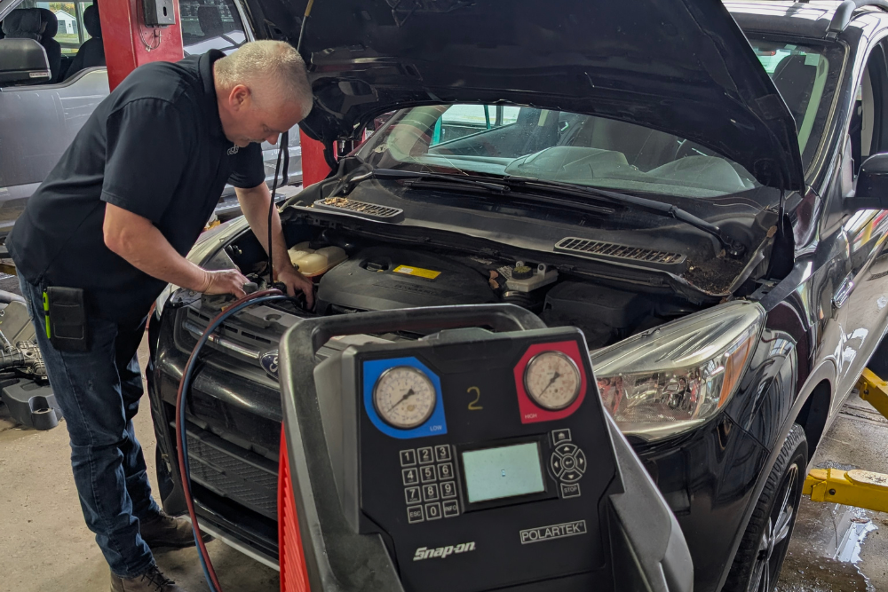 Grand Pointe Automotive Announces Early Summer Diagnostics Initiative for Vehicle Air Conditioning Systems. Image of a technician performing A/C service on a car