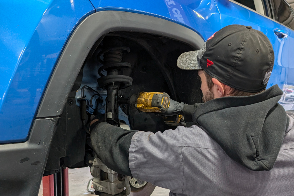 Suspension Repair in Flint & Burton, MI at Grand Pointe Automotive. Mechanic using an impact driver to repair a car's front suspension strut.